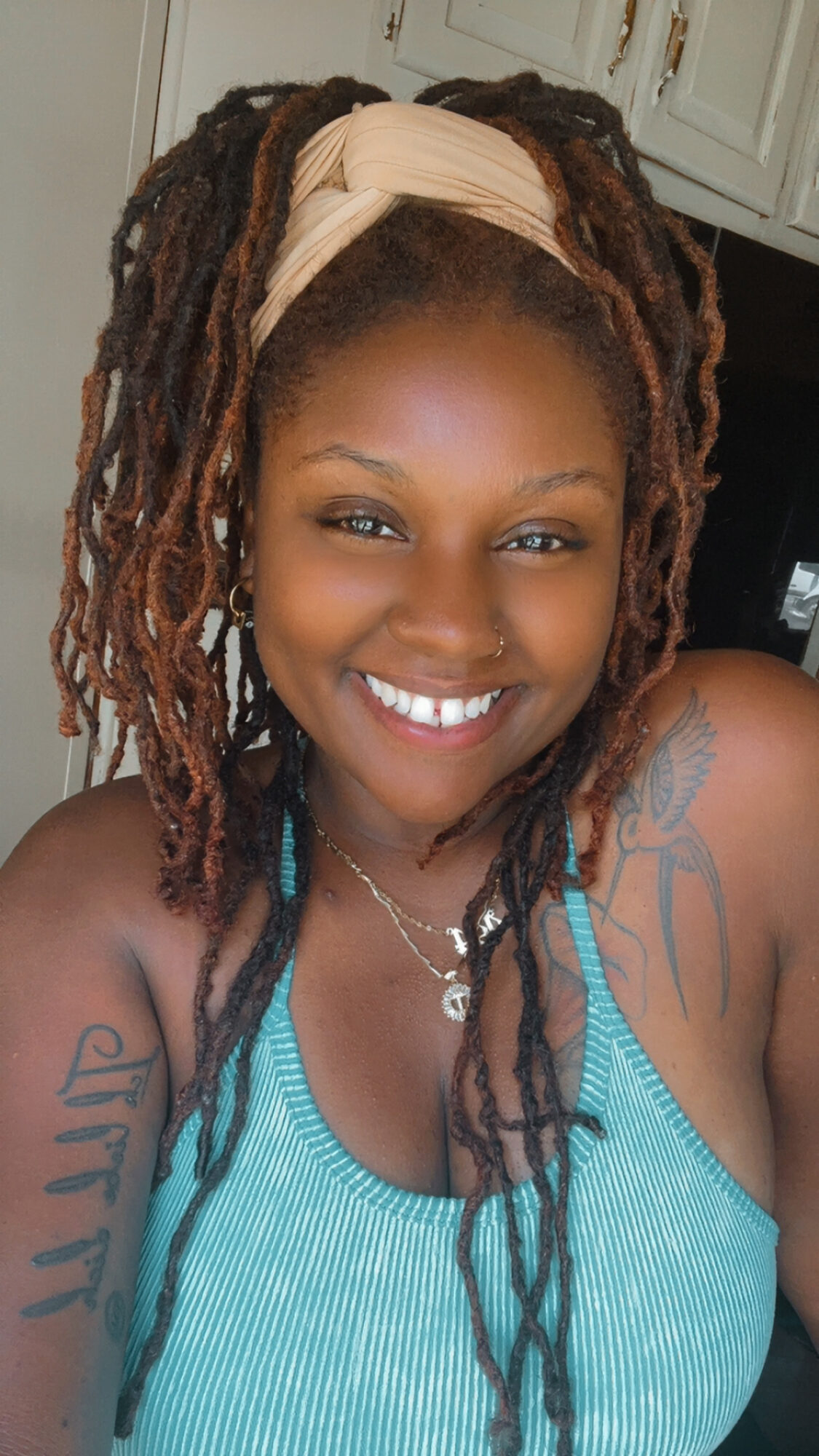 Smiling woman with dreadlocks, wearing a beige headband and a blue top, in a kitchen setting.