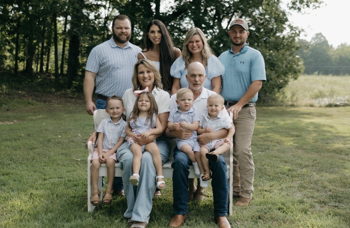 Group of ten people, including children and adults, outdoors on grass with trees in background.