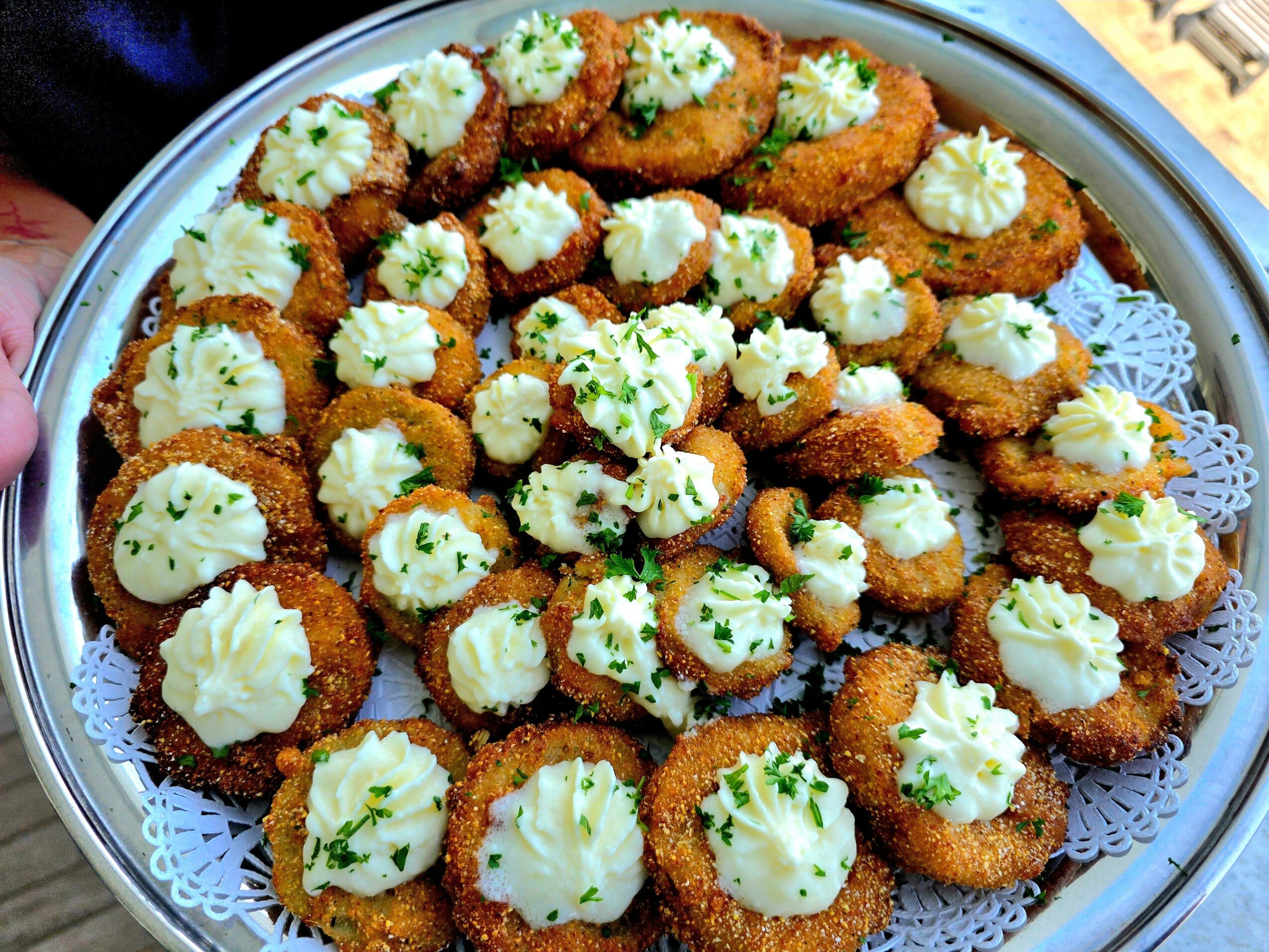 Plate of breaded fried appetizers topped with dollops of white sauce and chopped herbs, arranged on a decorative tray.