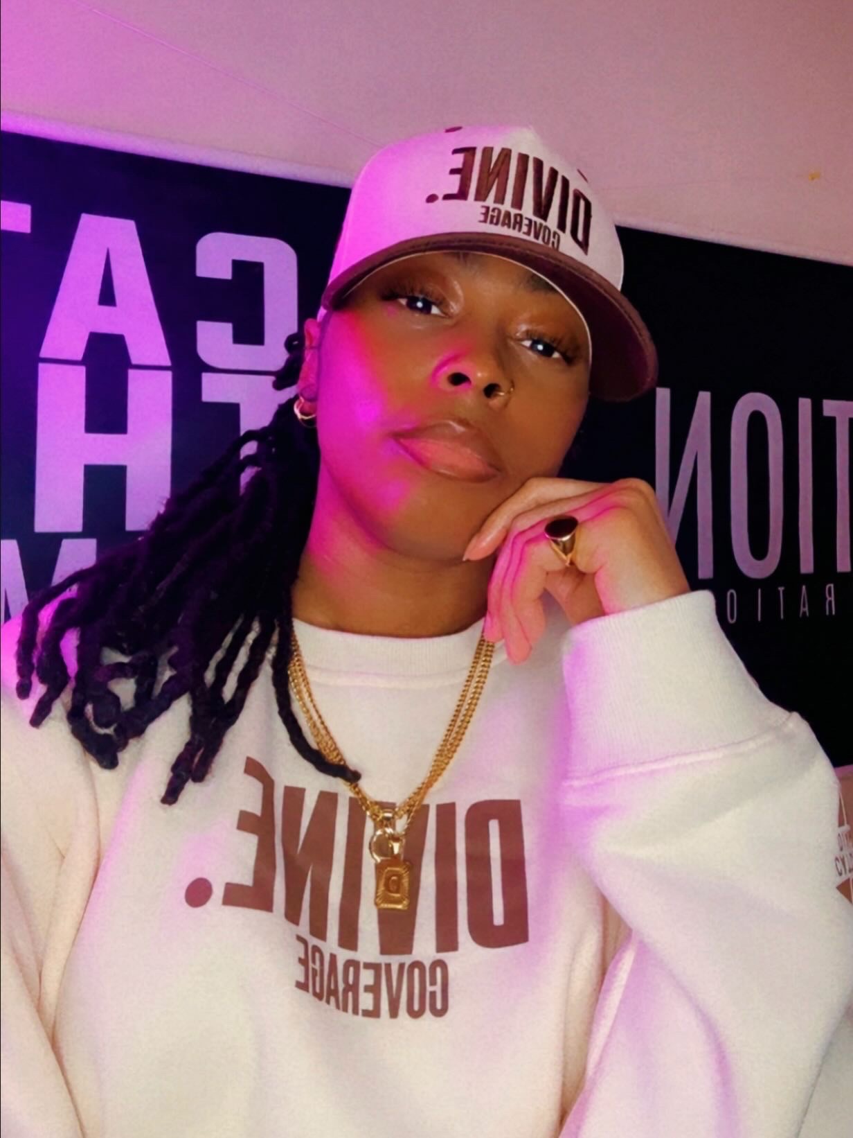 Person with long dreadlocks wearing a white cap and sweatshirt, posing with hand near face, background with text. 20 words.