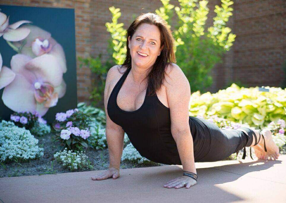 Woman doing a push-up outdoors with flowers and greenery in the background.