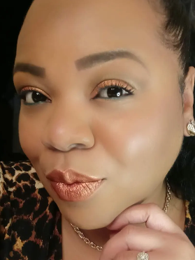 Close-up of a woman with makeup, wearing leopard print clothing and jewelry, touching her chin with her hand.
