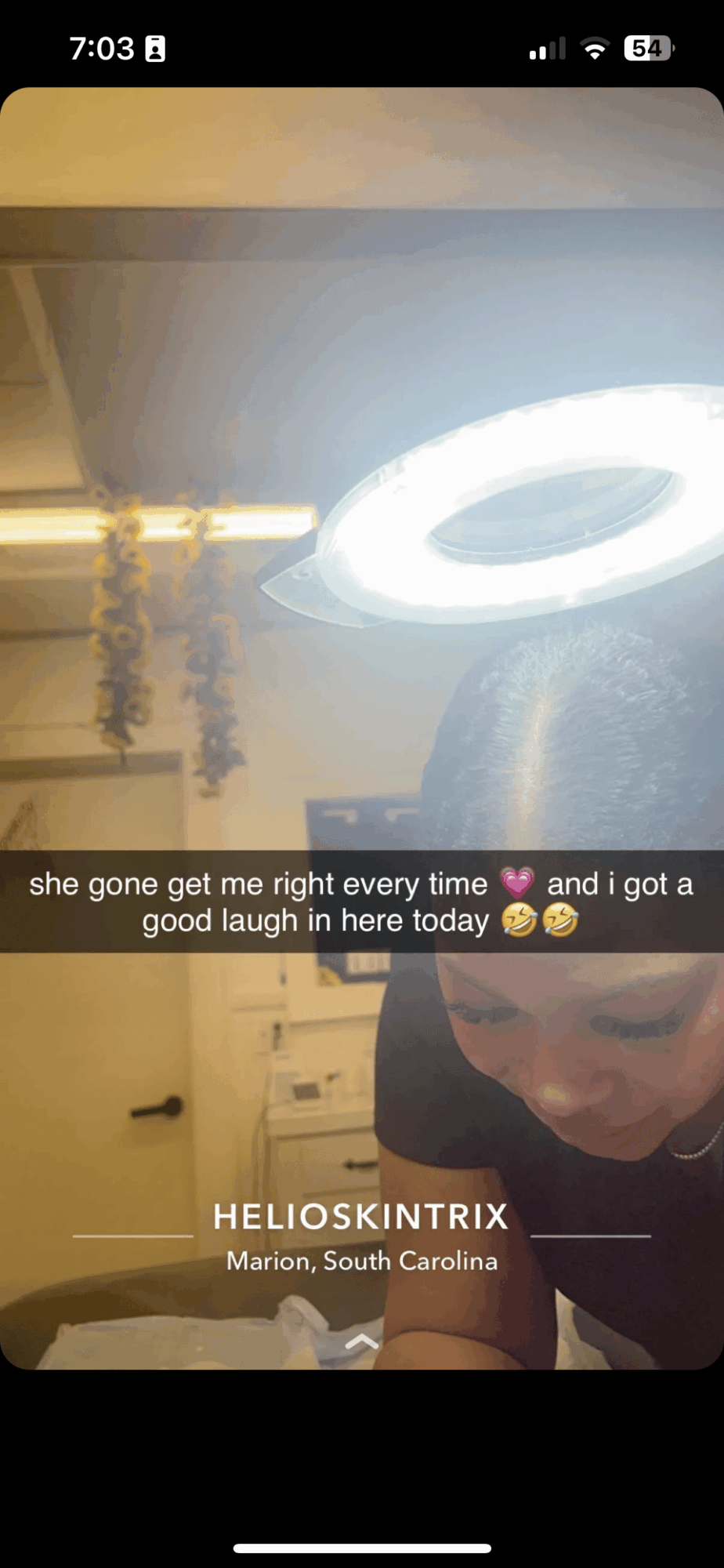 Person smiling in a room with a bright circular light fixture overhead, text overlay, and location information.