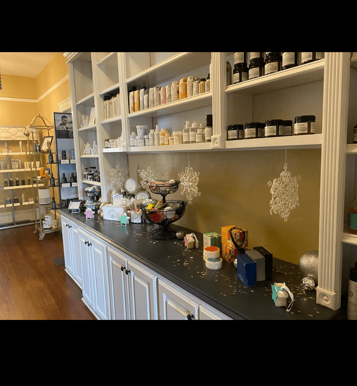 Shelves filled with jars and bottles, black countertop with various items, yellow wall, wooden floor.