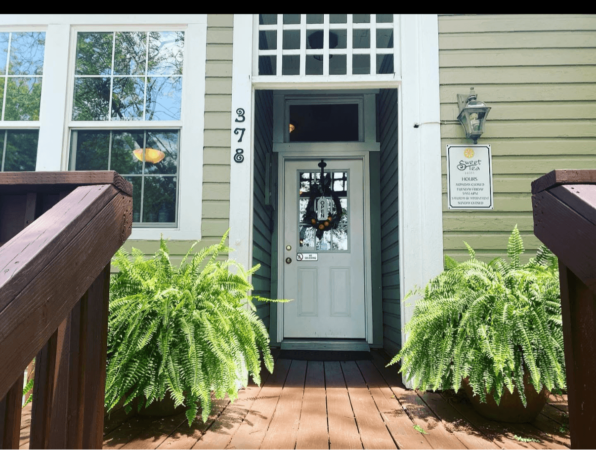 Front door with wreath, flanked by ferns, house number 978, and a lantern-style light fixture, with a sign on the wall.