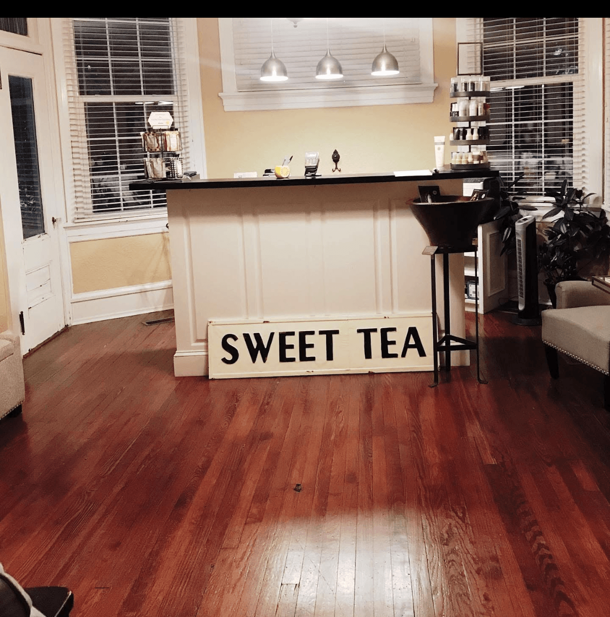 Living room with a bar area, sign reading 'SWEET TEA', hardwood floor, and large windows with blinds.