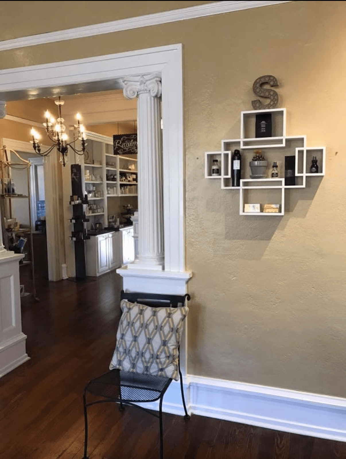Interior room with a chair, wall shelf, and doorway leading to a dining area with chandelier, bookshelves, and decor.
