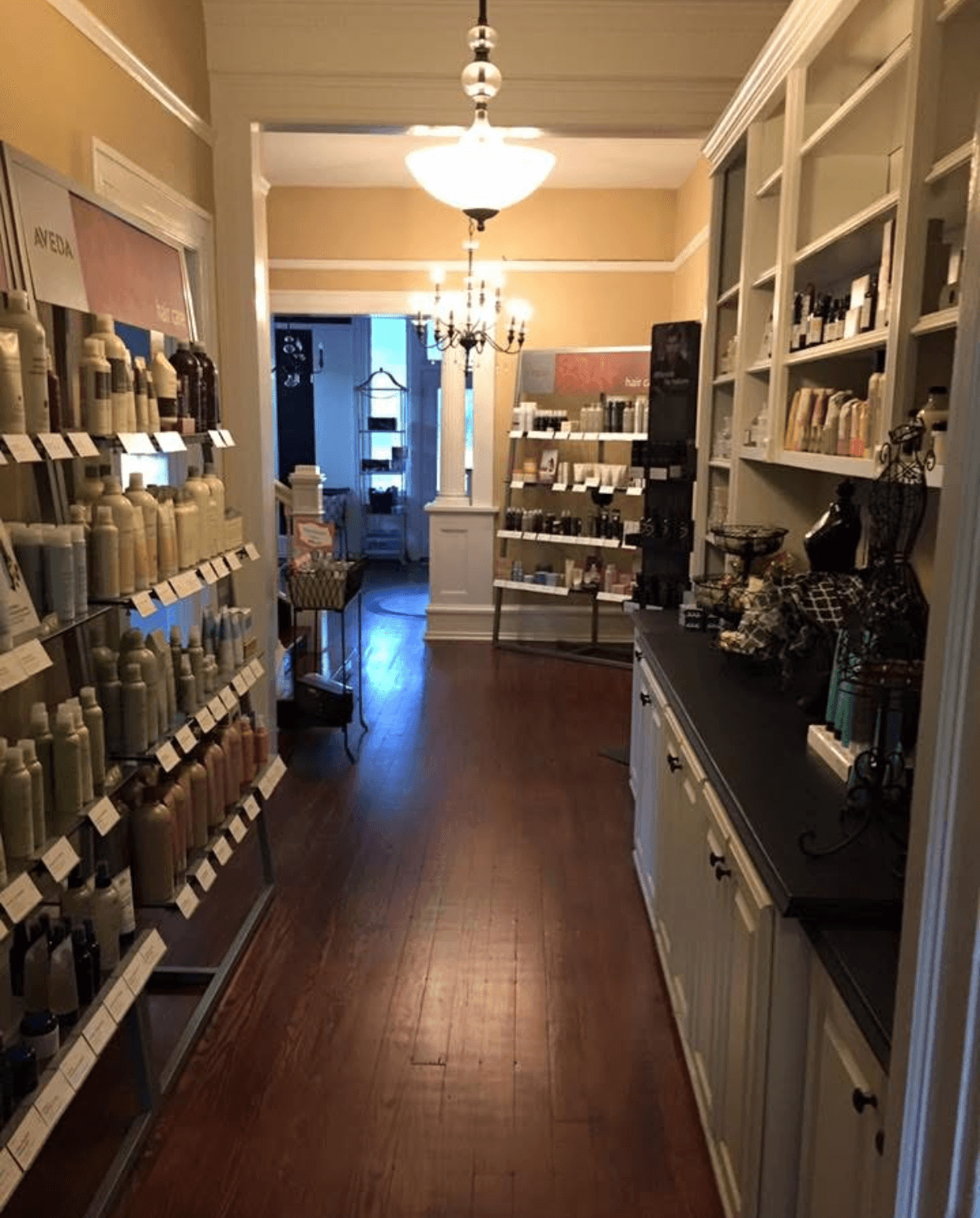Interior of a store with shelves stocked with products, a wooden floor, and a chandelier hanging from the ceiling.