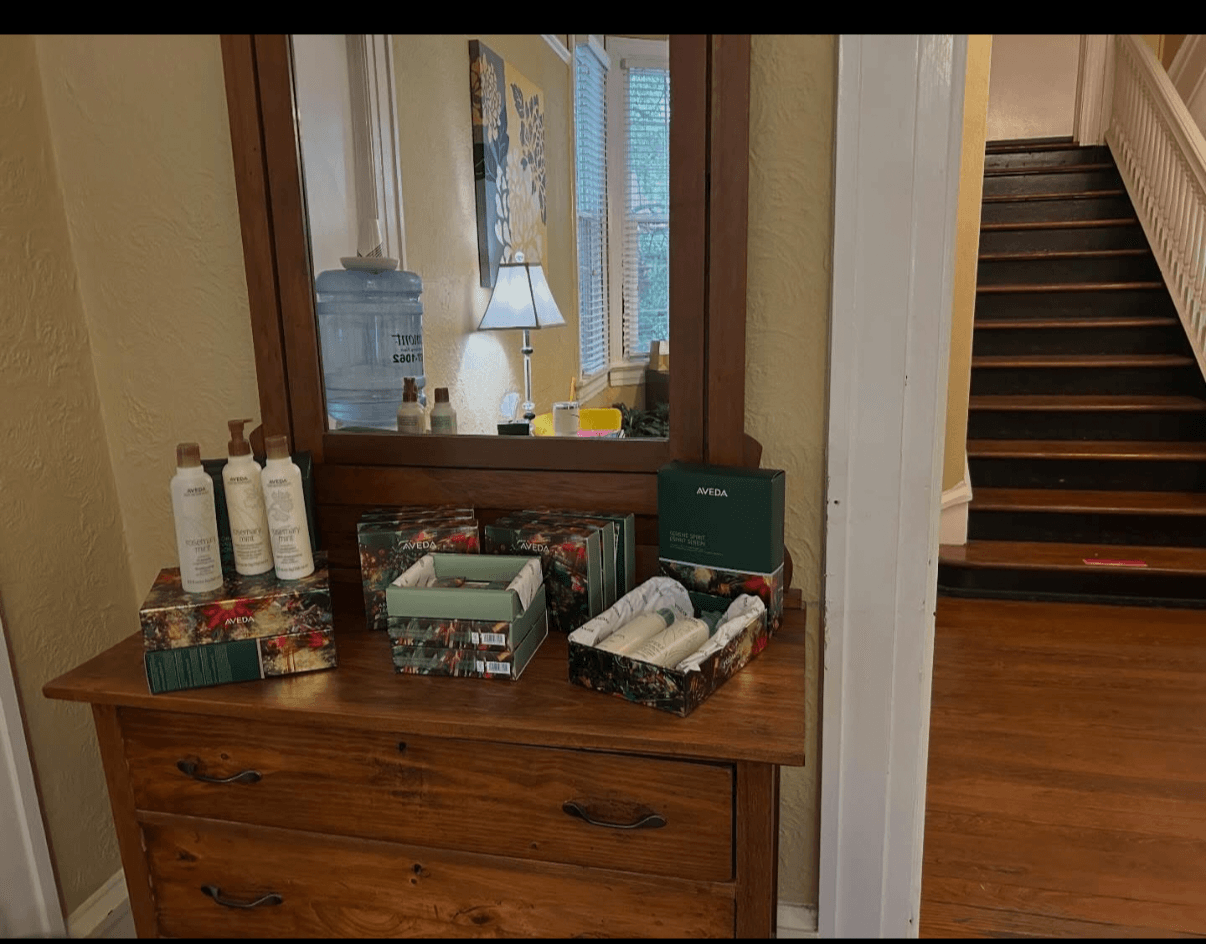Wooden dresser with bottles, boxes, and towels, mirror reflecting a lamp and window, staircase with dark steps nearby.