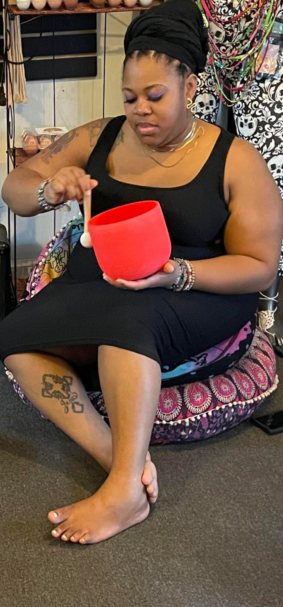 Woman sitting on a cushion, holding a red container, with a tattoo on her ankle, in an indoor setting.