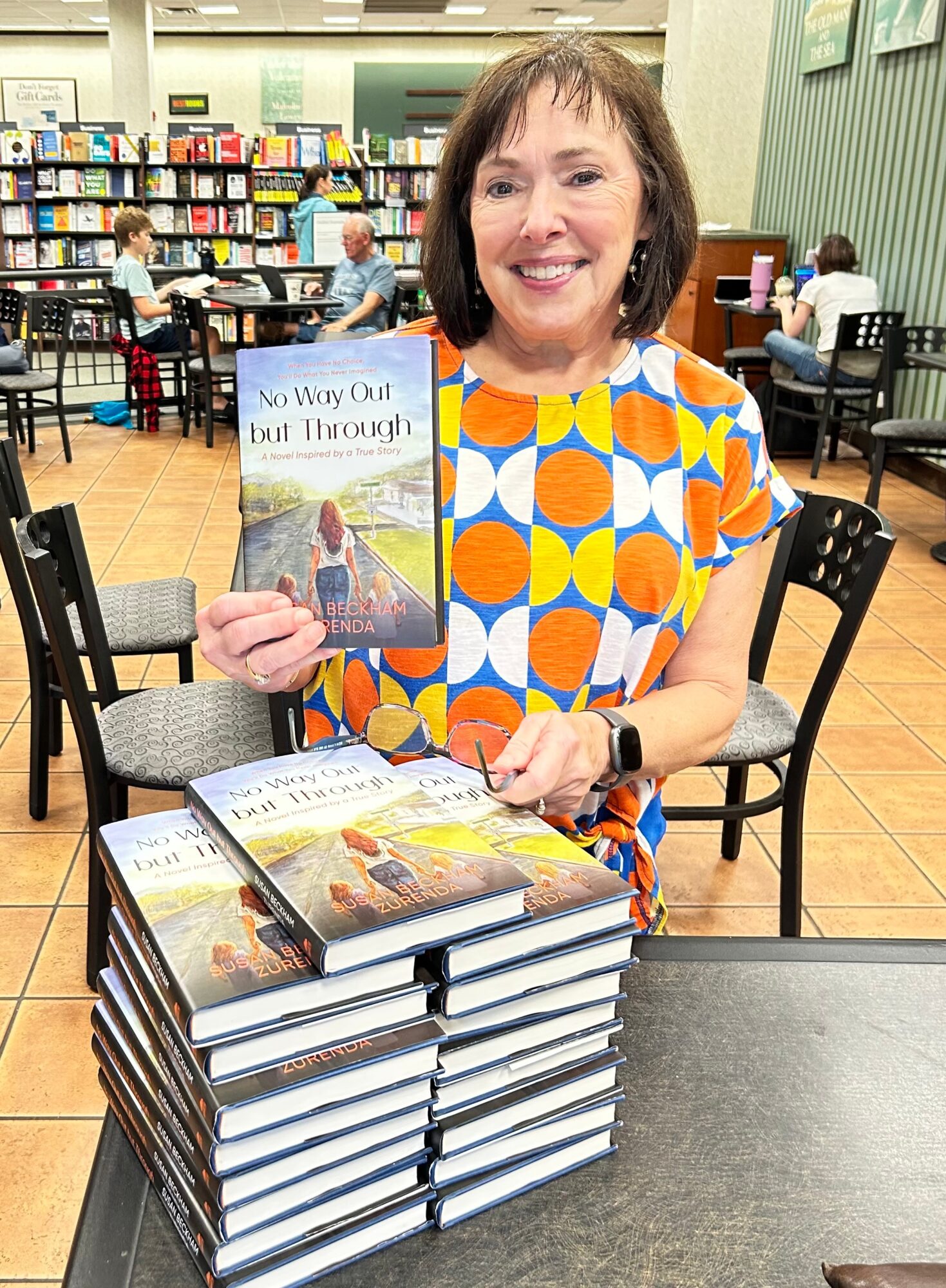 A person holds a book beside a stack of books in a library or bookstore.