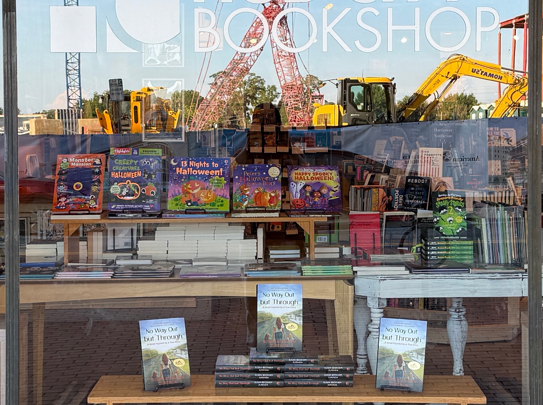 Bookshop window display with books and construction equipment reflected in the glass.