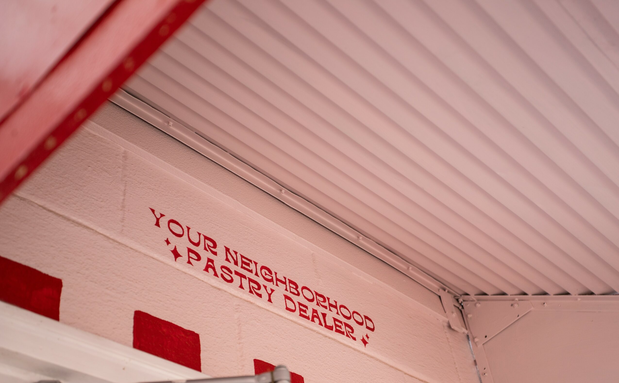Ceiling with a sign reading 'Your neighborhood pastry dealer?' in red text, angled and partially visible.