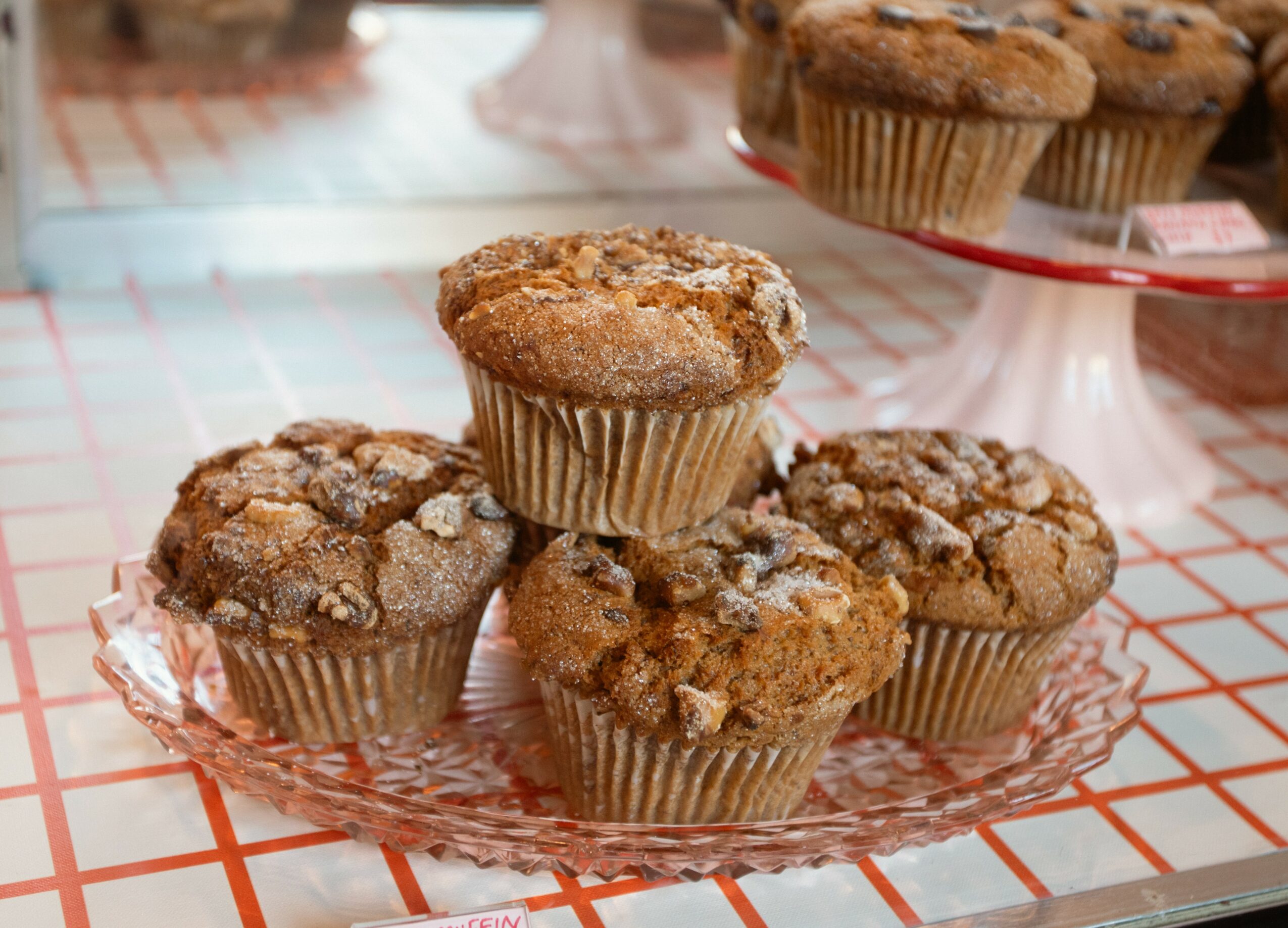 Five muffins on a glass plate with a red grid tablecloth background.