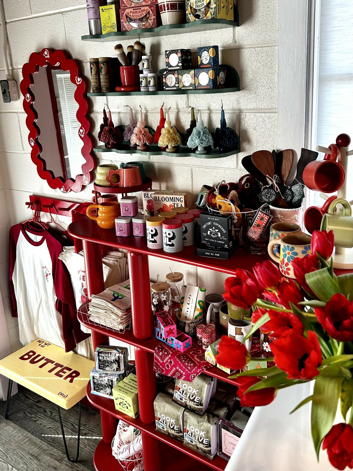 Shelves with various decorative items, a red mirror, and a bouquet of red flowers in a vase.