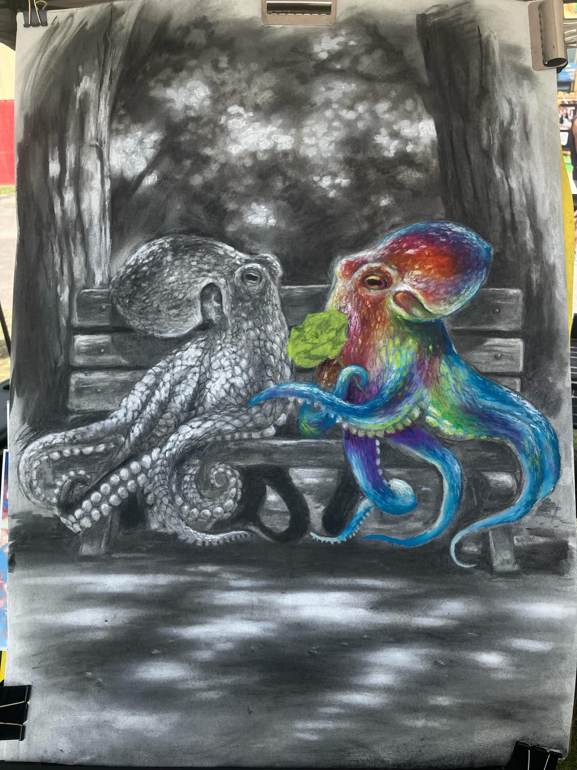 Colorful octopus and gray octopus sit on a park bench under a cloudy sky, engaging with each other.