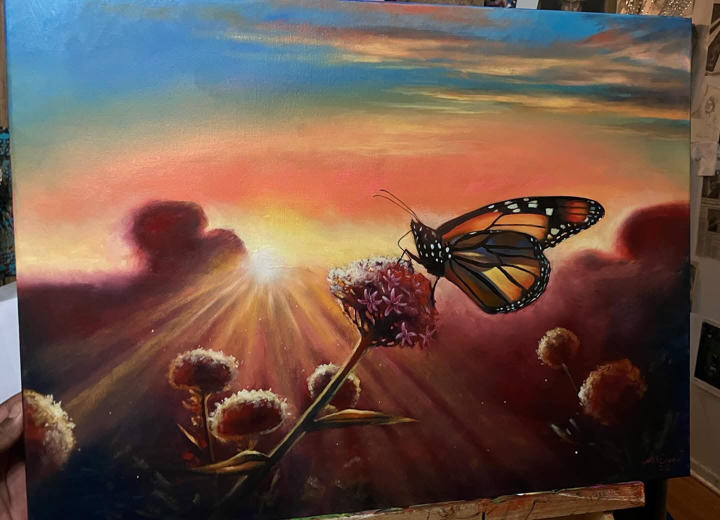 Butterfly on a flower with a sunset sky and clouds in the background, warm colors, and blooming plants.