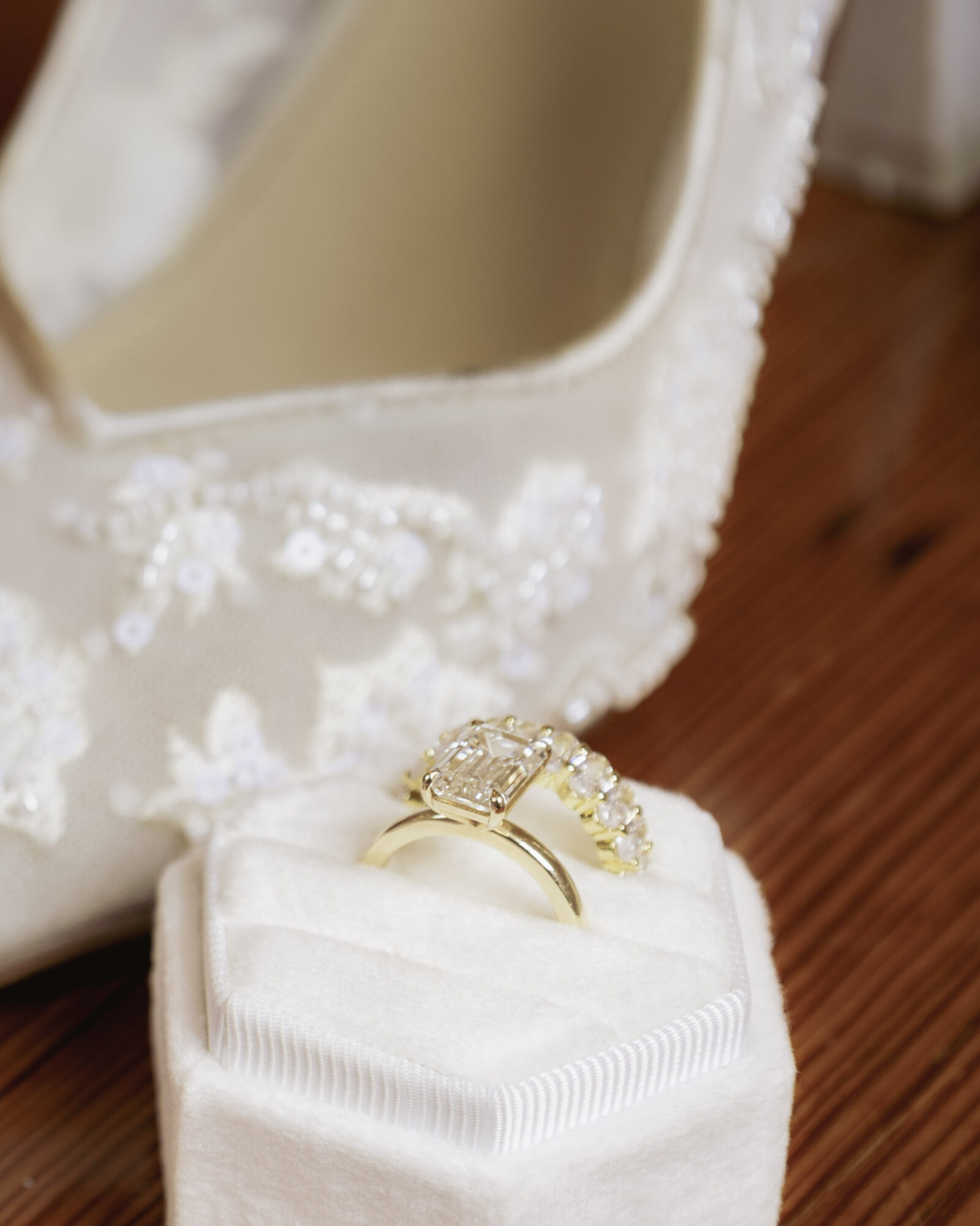 Gold ring with a large central gemstone and smaller surrounding stones, placed on a white cushion inside a decorative box.