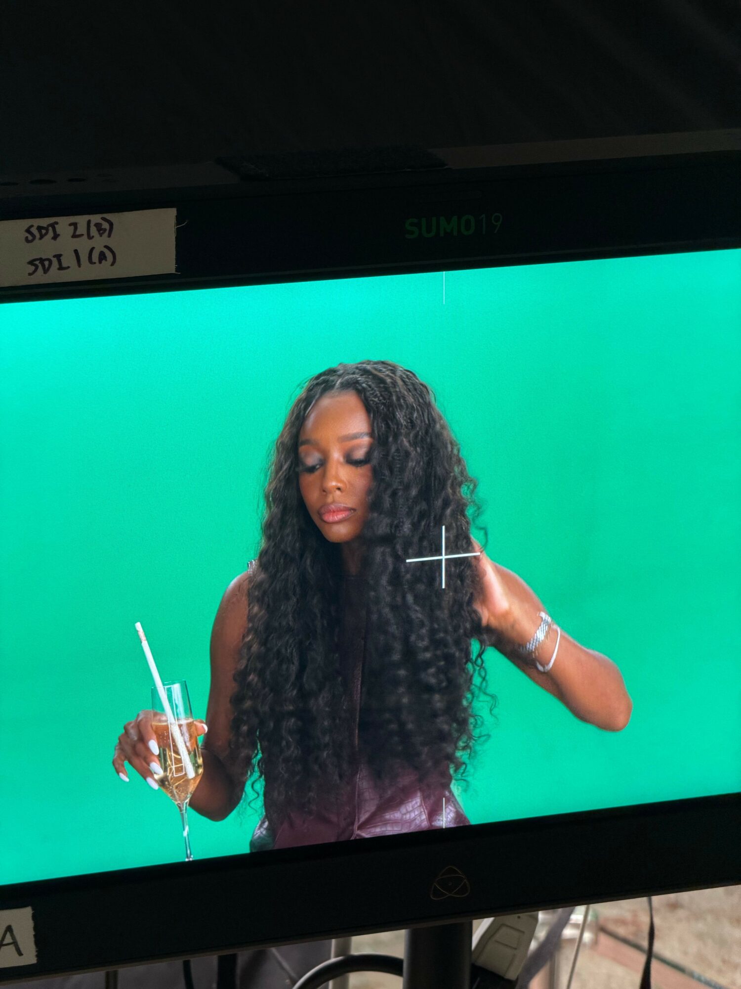 Woman with long curly hair holding a phone, facing left, against a green background.
