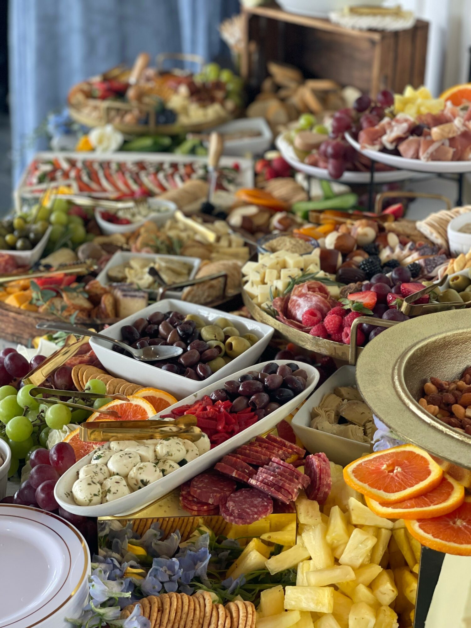 Assorted fruits, cheeses, meats, and snacks arranged on a table for a buffet or party spread.