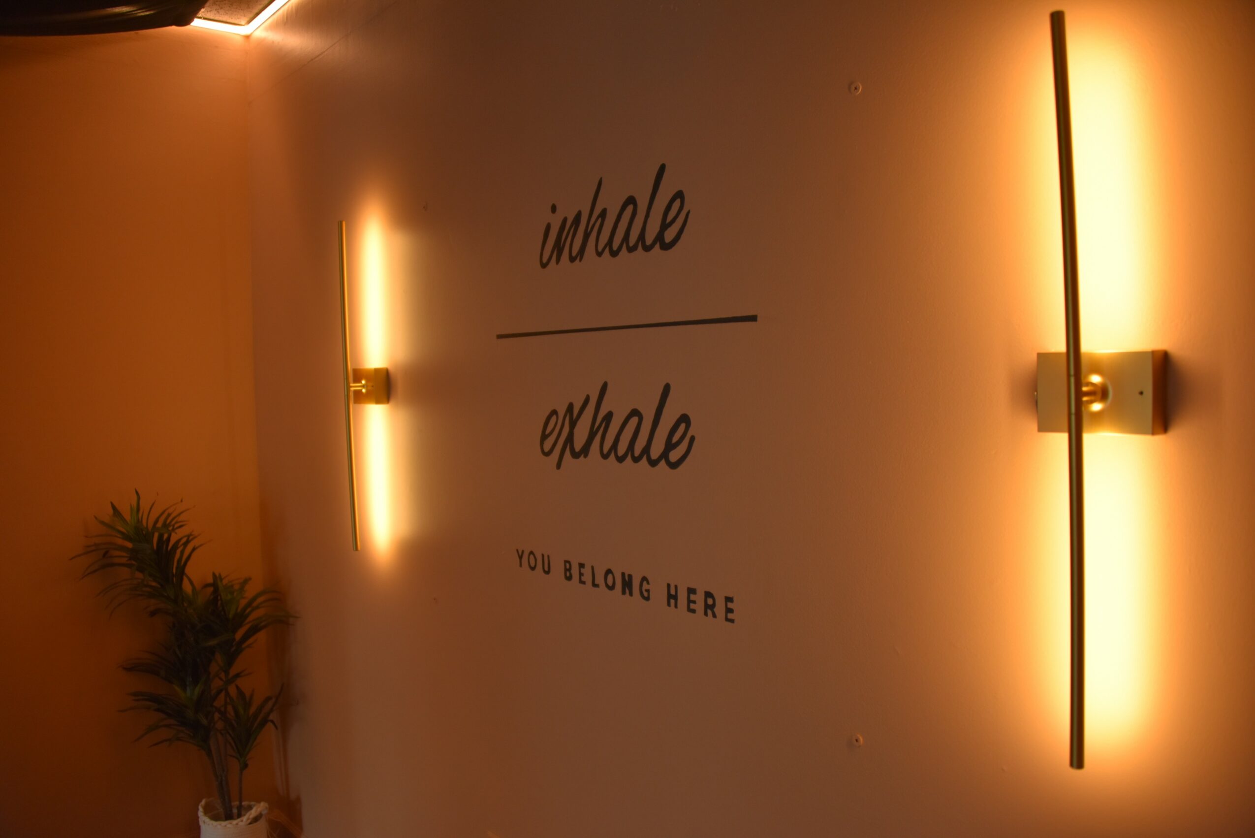 Wall with illuminated text reading 'inhale' and 'exhale', and a small plant on the left, warm lighting, and a modern wall sconce.