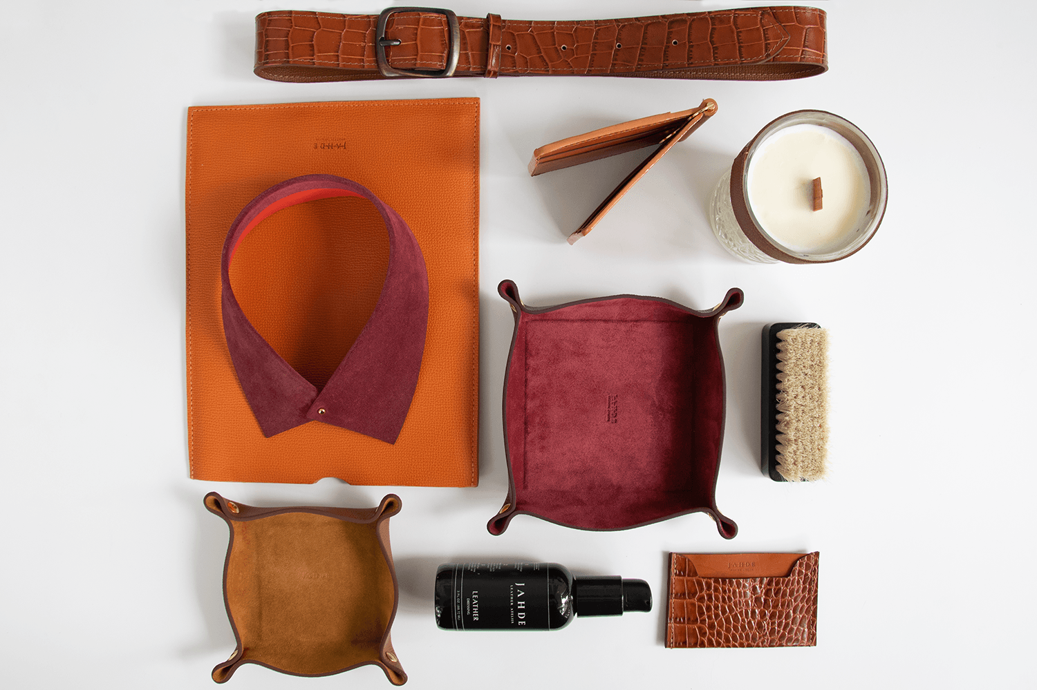 Flat lay of various objects including a belt, notebook, candle, hairbrush, and wallet on a white background.