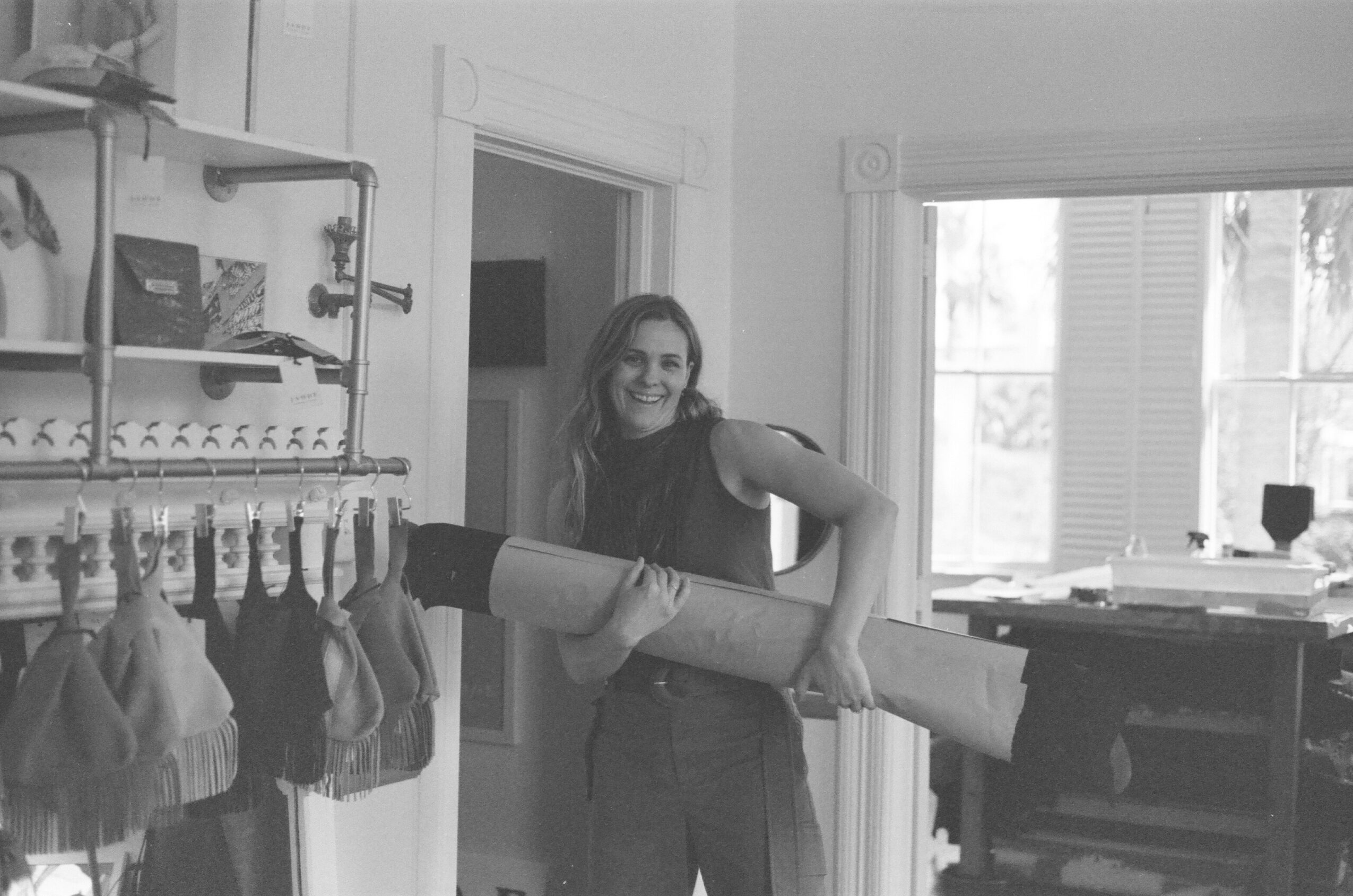 Woman holding a rolled-up poster in a room with windows and shelves, smiling at the camera.