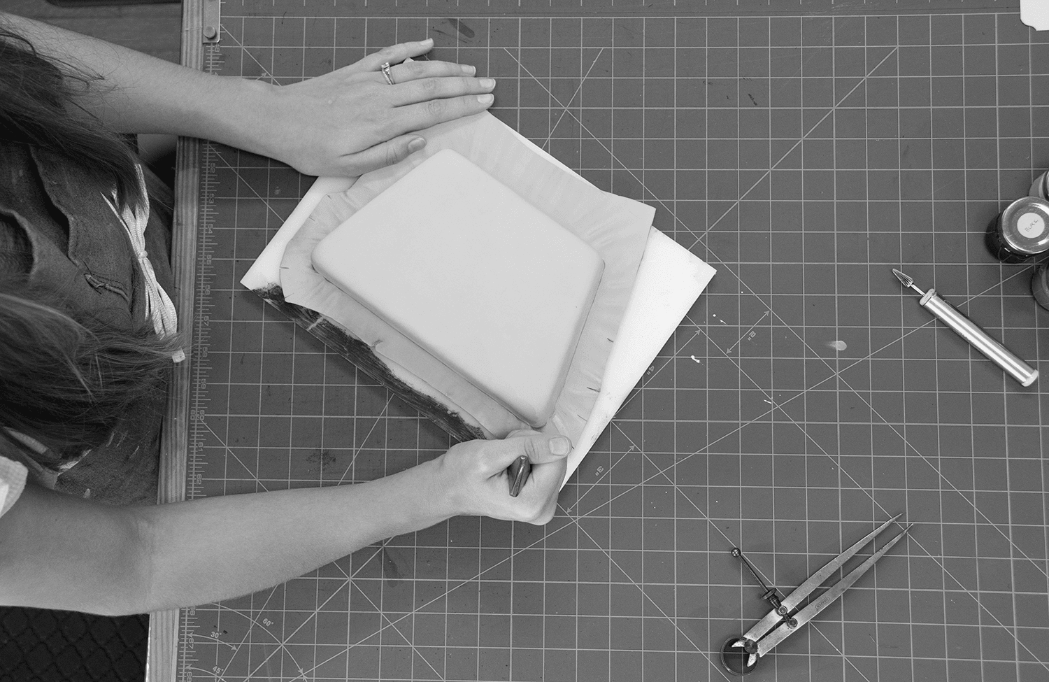 Person working on a craft project with tools and materials on a cutting mat, viewed from above.