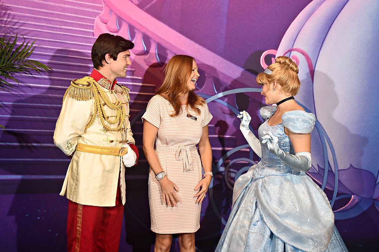 A person in a white uniform and red trousers, a woman in a pale dress, and a person in a blue gown stand together indoors.