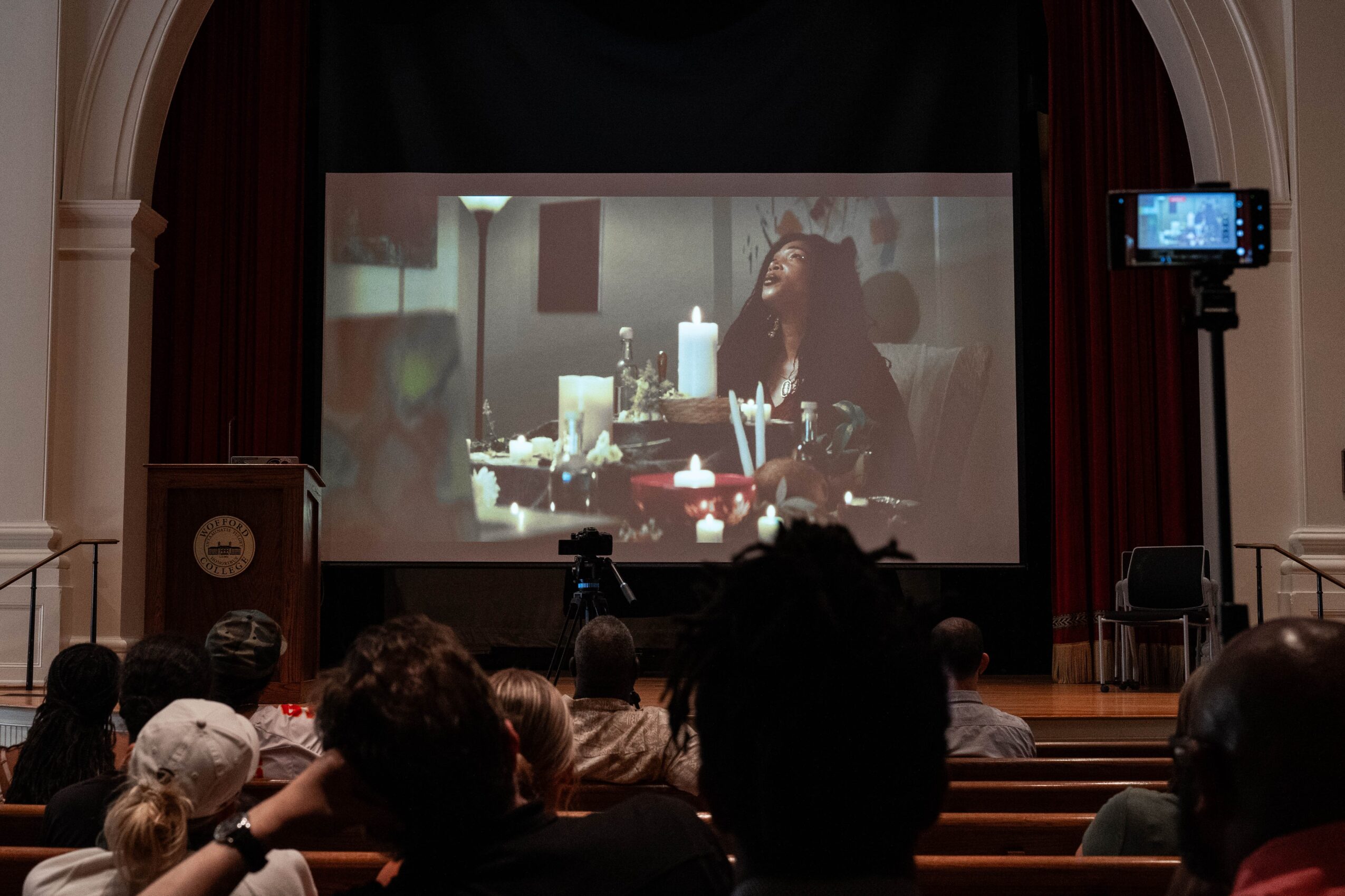 Audience seated in a theater watching a film projected on a screen.