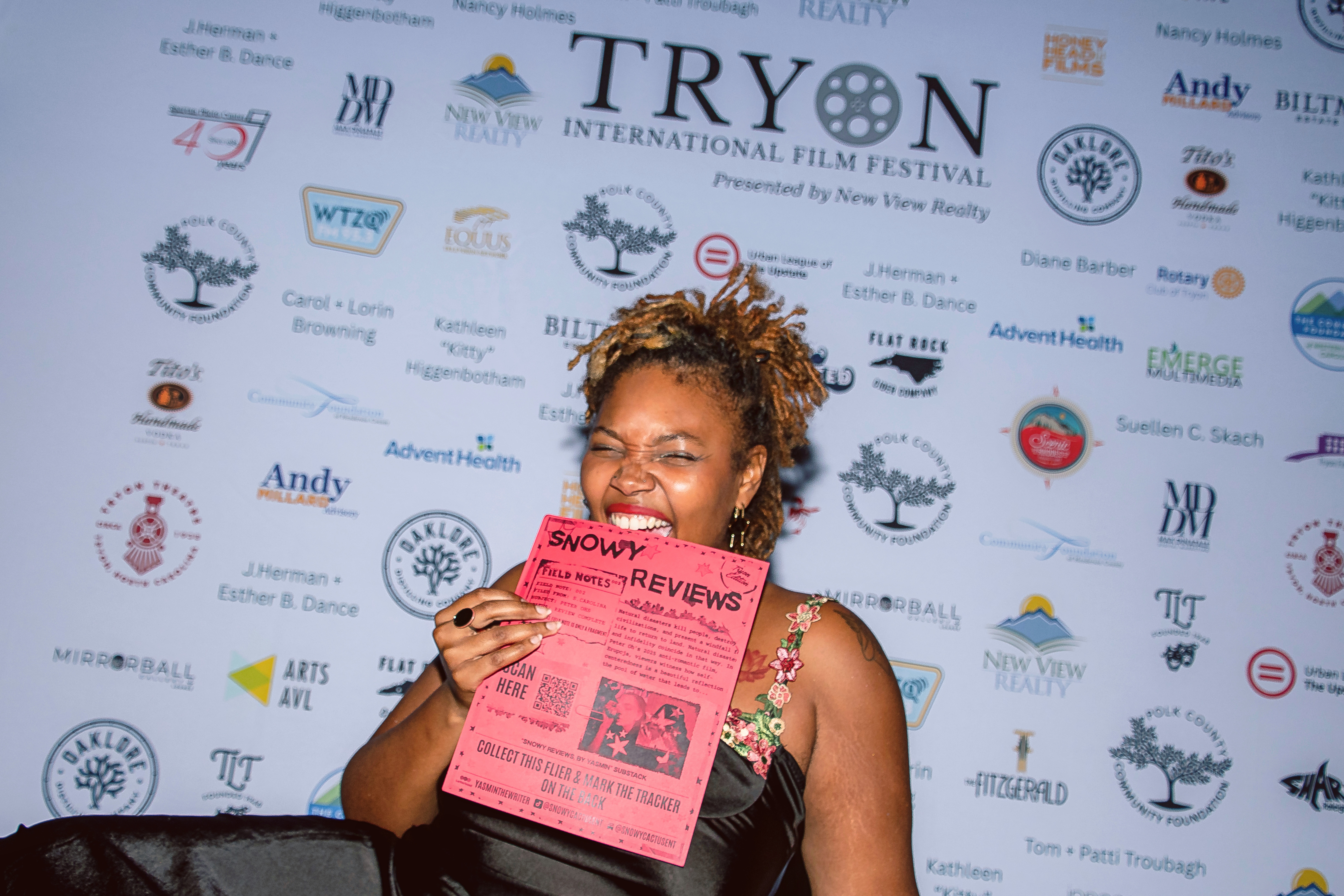 Person holding a pink review sheet in front of a sponsor-logo backdrop.
