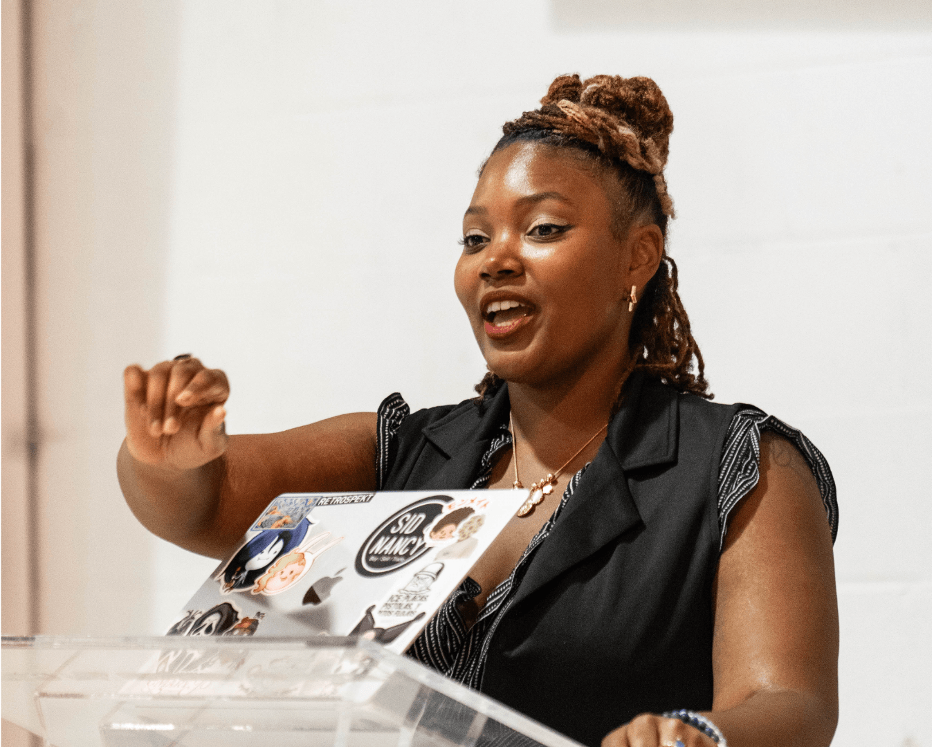 A person speaks behind a clear lectern with a laptop open in front of them.