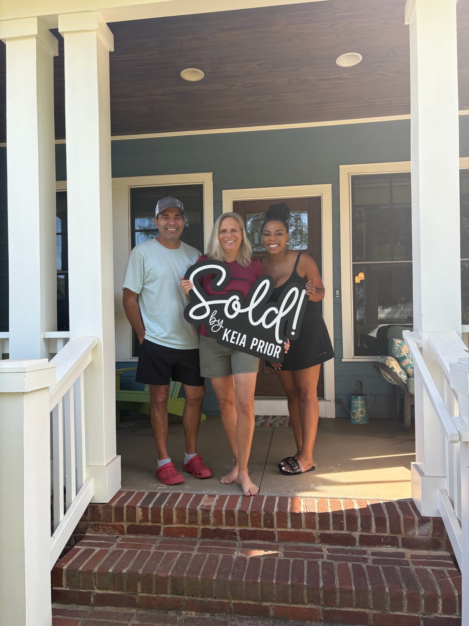 Three people pose together on a brick porch beneath a sign reading “Sole! by KEIA PRIOR.”