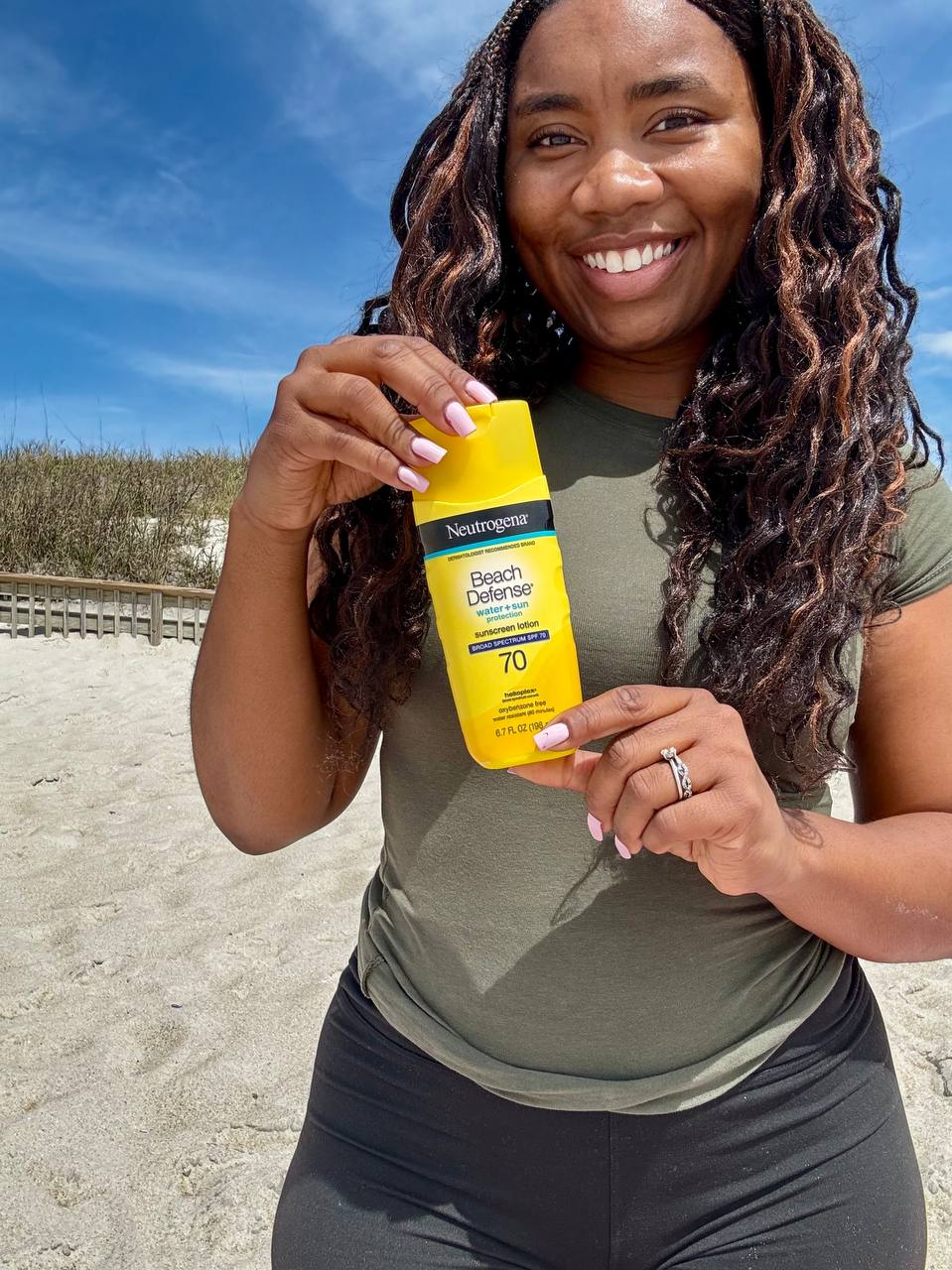 Person holding a yellow sunscreen bottle on a sandy beach.